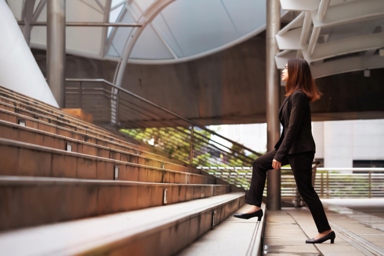 Professionally dressed woman walking up stairs of a building exterior