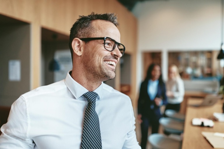 Laughing mature businessman standing in an office before a meeting with a diverse group of work colleagues